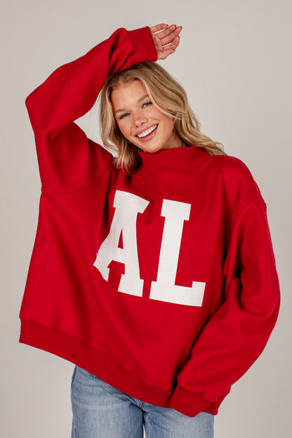 A smiling blonde woman wearing an oversized red sweatshirt with large white block letters &