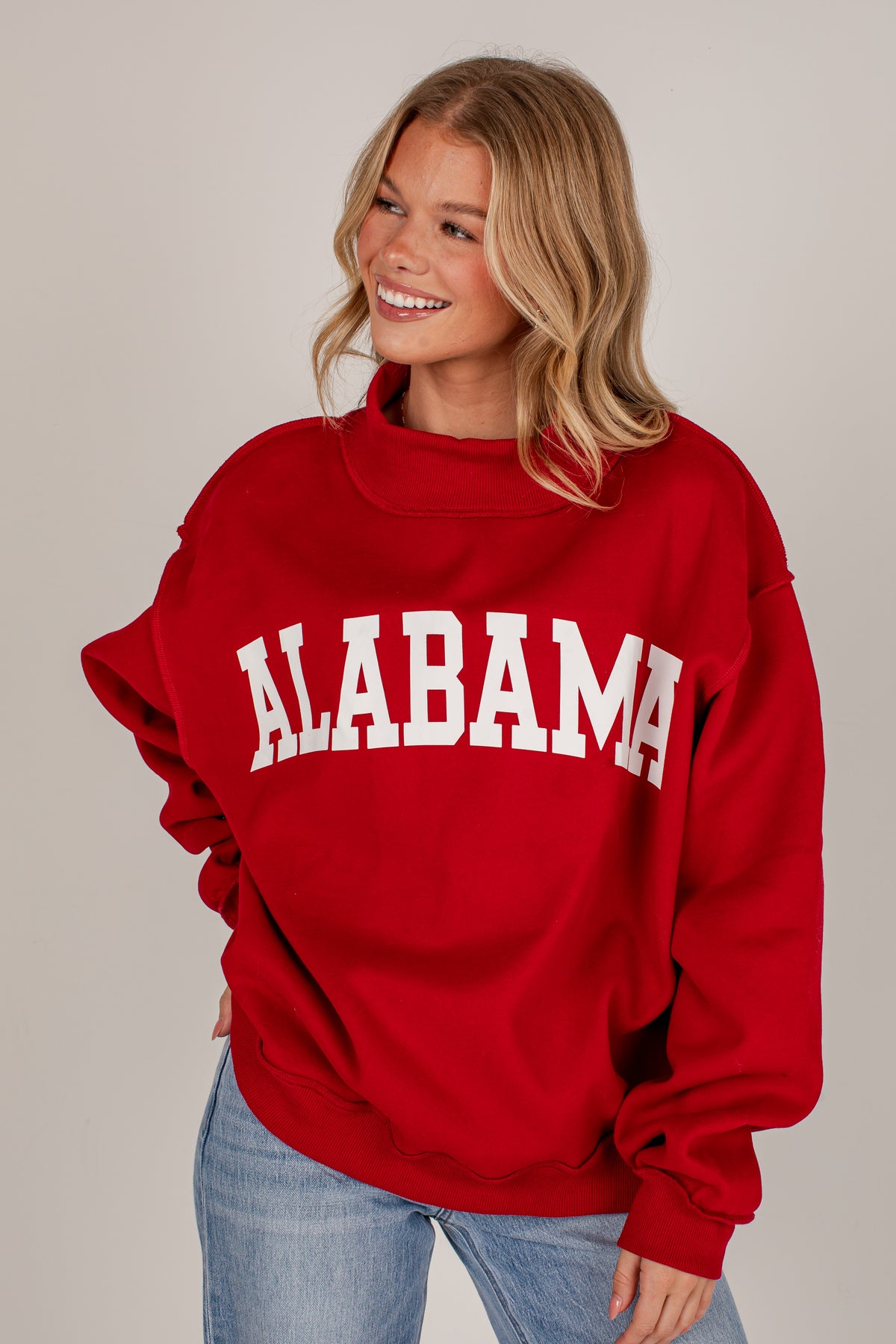 A smiling blonde woman wearing a red sweatshirt with &