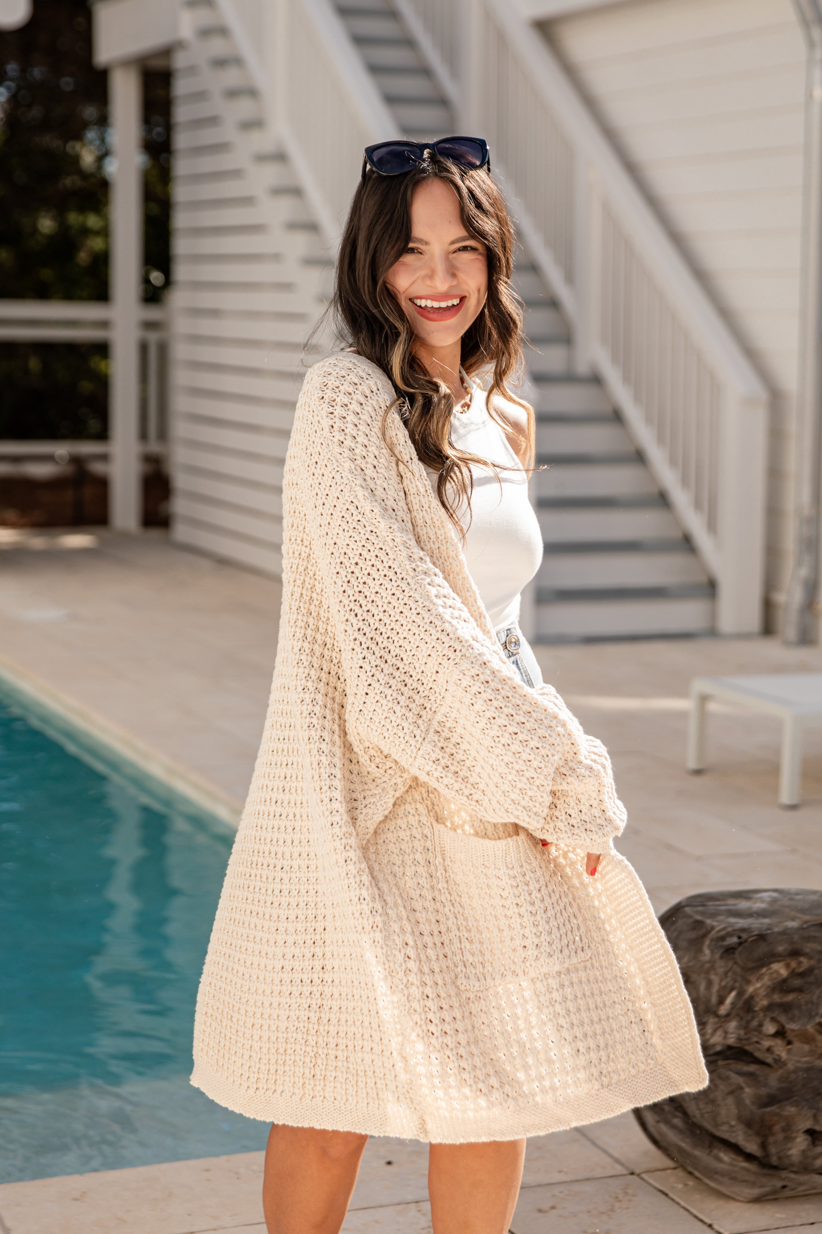 Woman in a beige cardigan standing by a poolside