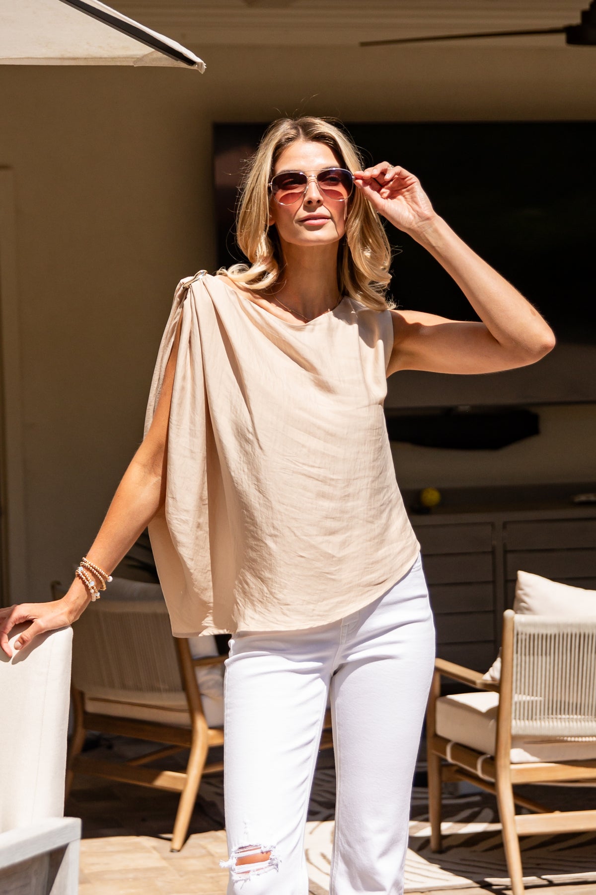 Woman wearing a beige top and white pants on a patio