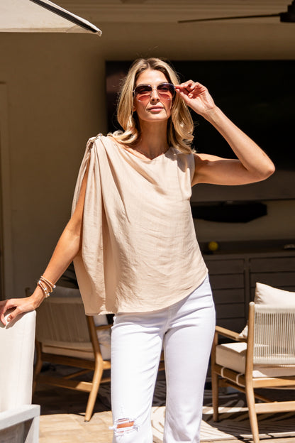 Woman wearing a beige top and white pants on a patio