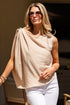 Woman wearing a beige sleeveless top and white pants outdoors.