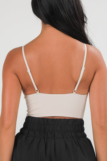 Person wearing a beige tank top with thin straps on a plain background