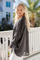 Woman wearing a dark gray cardigan over a light top on a balcony with a blurred background
