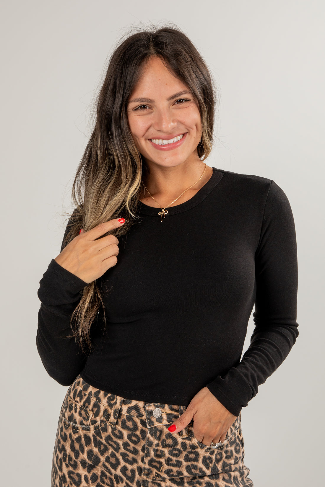 Woman wearing a black long-sleeve top and leopard print skirt on a plain background
