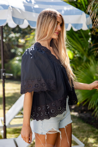 Woman wearing a black lace top and denim shorts standing outdoors under a blue and white striped umbrella.