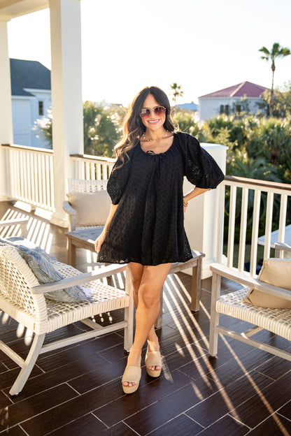 Woman in a black dress standing on a balcony with chairs and a scenic background