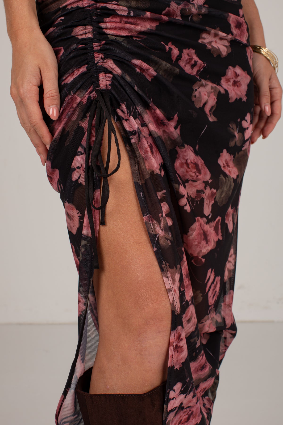 Close-up of a ruched black sheer skirt with a pink floral print and a side tie detail, worn by a model.