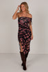 A woman modeling a strapless black mesh dress with a pink floral print, side tie details, and a high side slit, paired with dark brown knee-high boots against a plain light gray studio background.