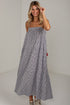 A woman modeling a sleeveless, tiered maxi dress with a small black and white gingham pattern, paired with beige sneakers, in a bright studio setting.