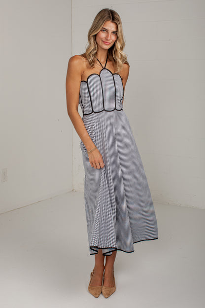 A woman modeling a sleeveless halter midi dress with a black and white striped pattern and black trim, standing in a white studio setting.