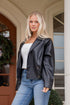 Woman wearing a black leather jacket and blue jeans standing in front of a building.