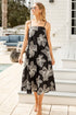 Woman in a black floral dress standing on a wooden deck by a poolside.