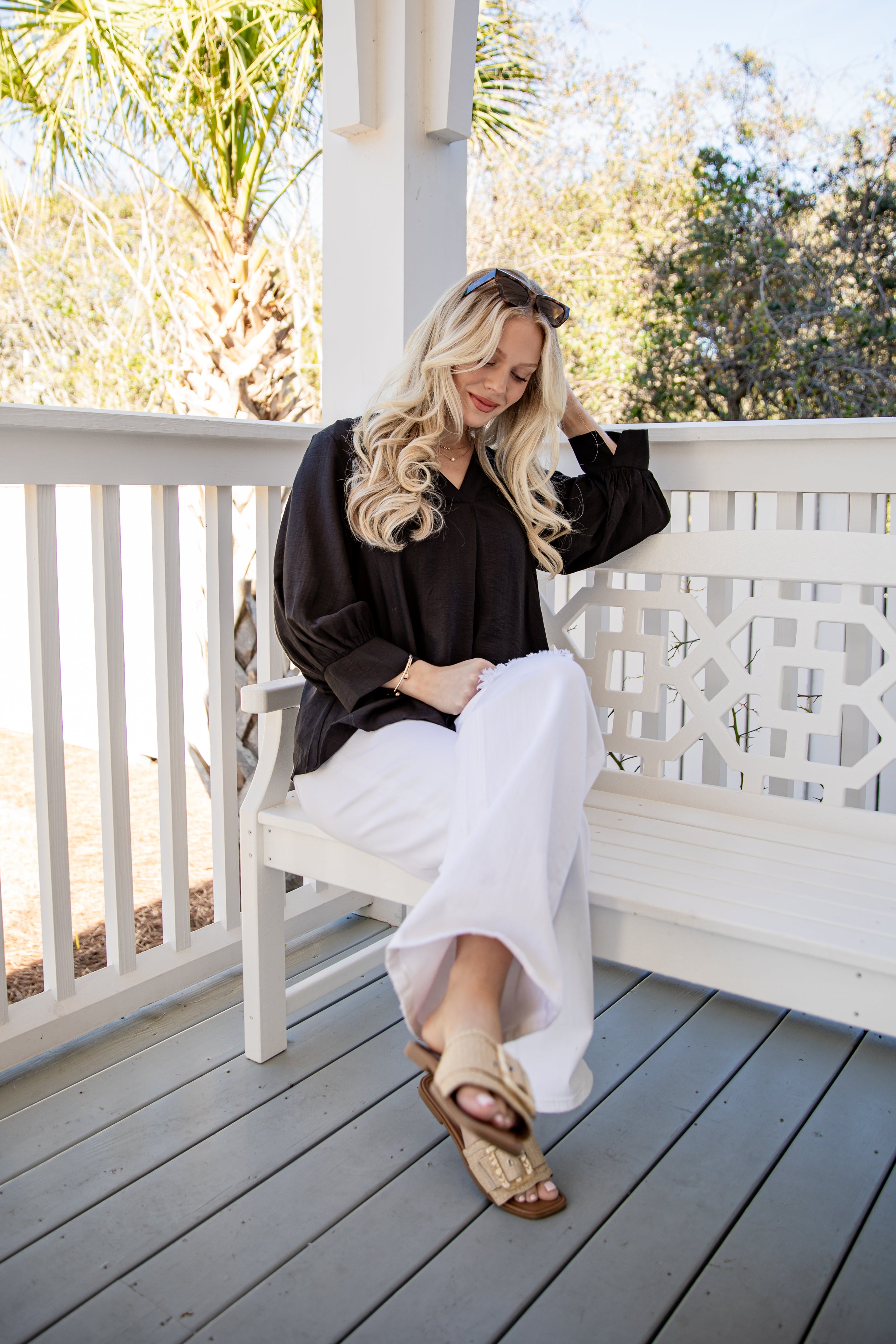 Woman sitting on a white bench on a wooden deck with trees in the background