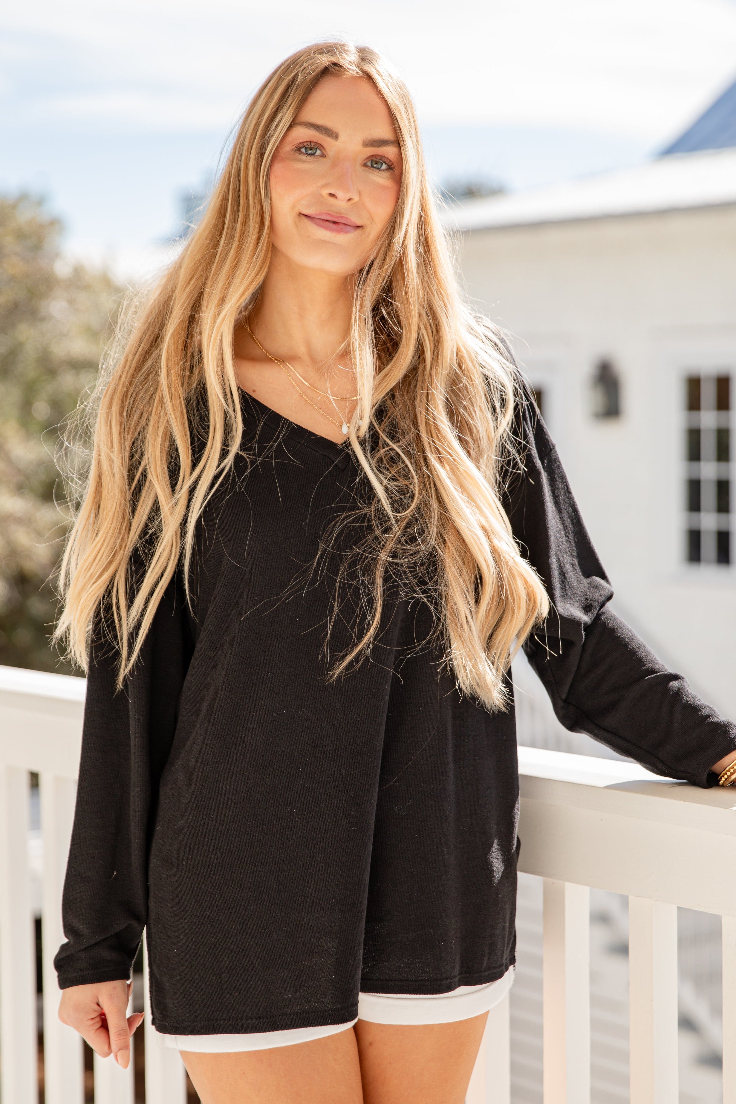 Woman wearing a black long-sleeve top and white shorts on a balcony.