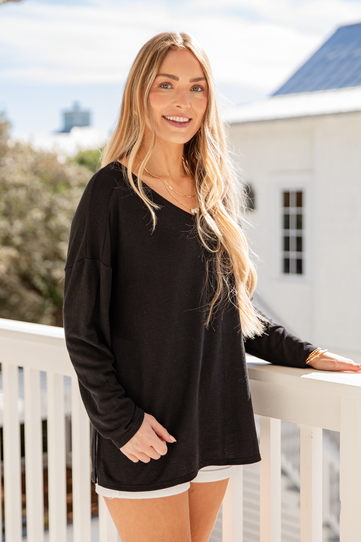Woman wearing a black long-sleeve top and white shorts standing on a balcony.