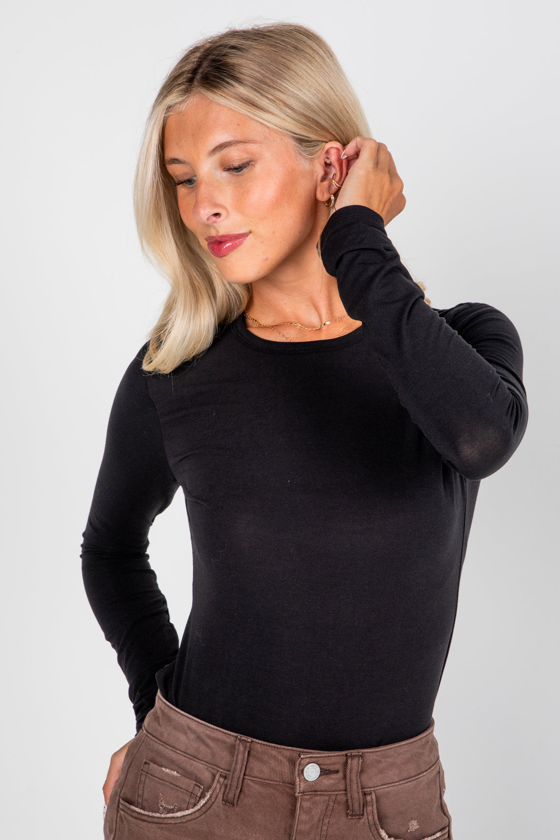 Woman wearing a black long-sleeve top and brown pants against a white background