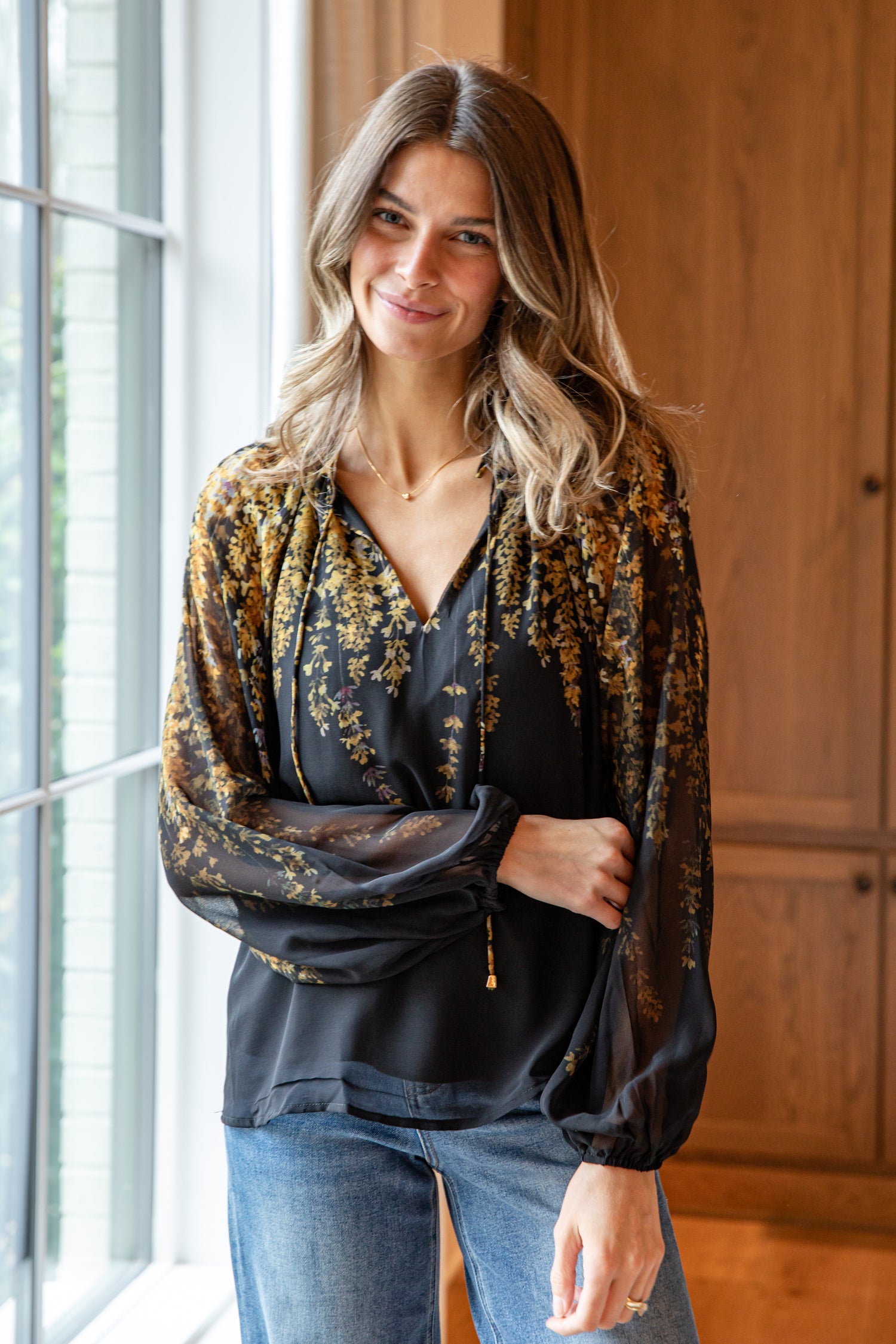 Woman wearing a floral blouse and jeans standing indoors.
