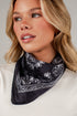A close-up of a woman wearing a black bandana with a white paisley pattern around her neck, paired with a white top against a neutral gray background.