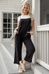 Woman in a black jumpsuit and white sneakers standing on a porch.