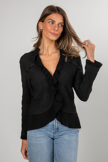Woman wearing a black blazer and blue jeans against a gray background