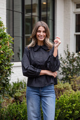 Woman wearing a black blouse and blue jeans standing outdoors.