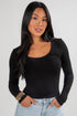 Woman wearing a black long-sleeve top and light blue jeans against a gray background