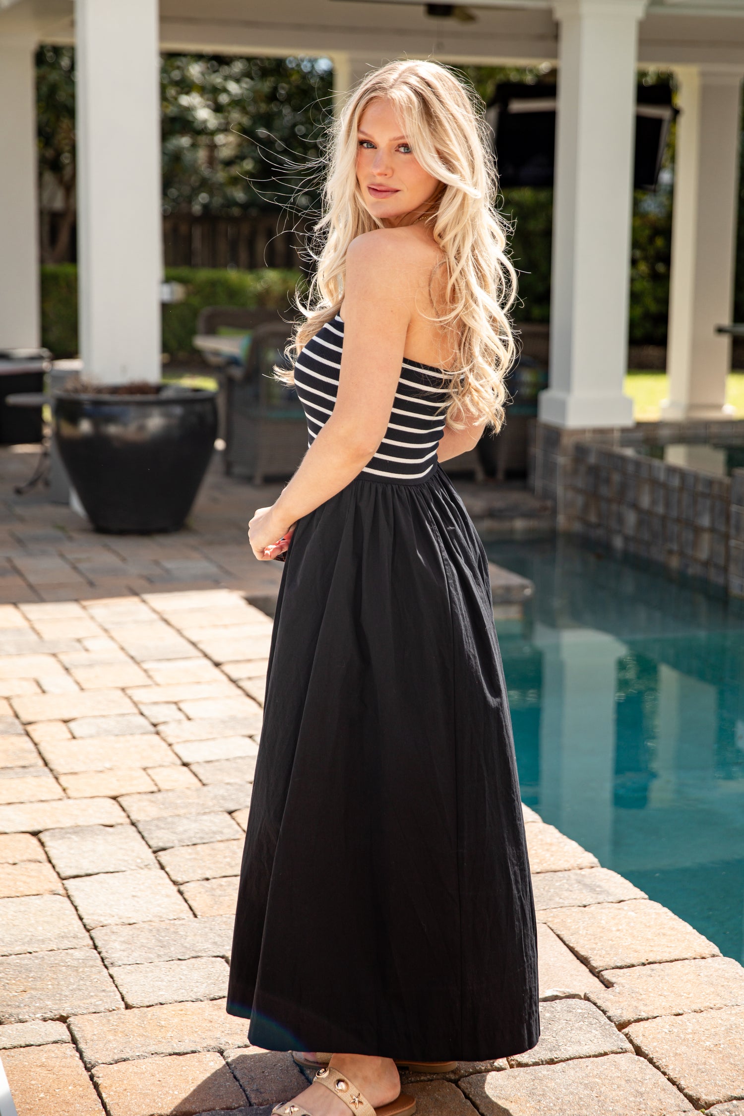 Woman in a black and white striped top and black skirt standing by a pool.