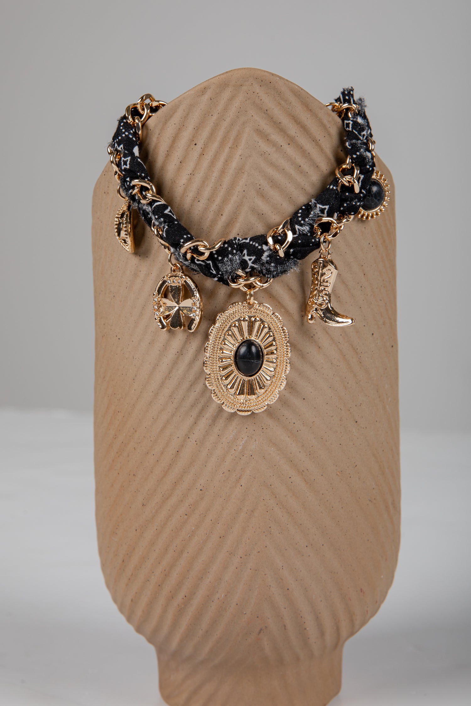 Bracelet with gold and black charms on a brown textured stand