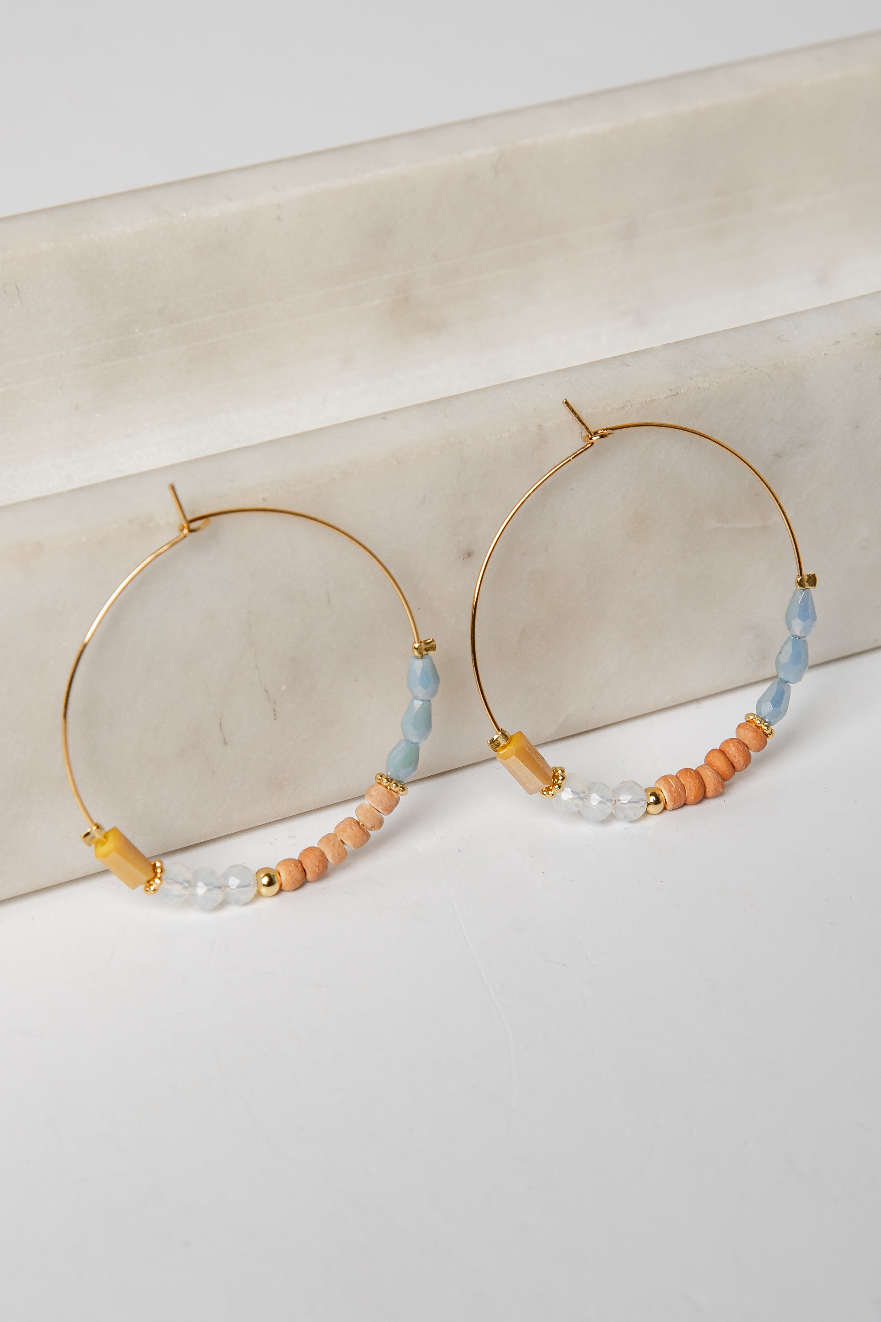 Gold hoop earrings with colorful beads on a light background