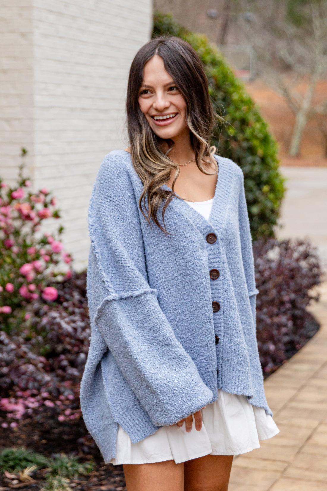 Woman wearing a light blue cardigan with brown buttons outdoors.