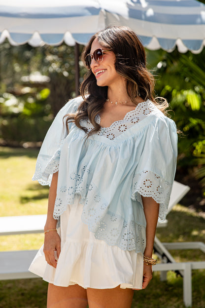 Woman wearing a light blue blouse with lace details and a white skirt outdoors.