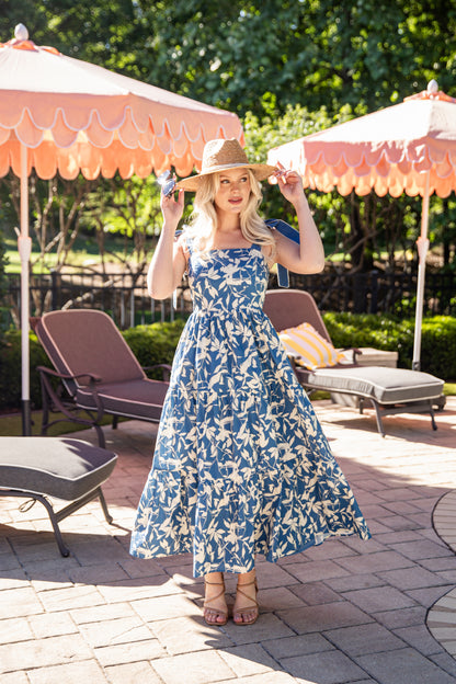 Woman in a blue floral dress standing under pink umbrellas on a patio.