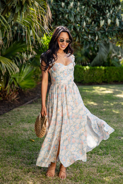 Woman in a floral dress standing outdoors with greenery in the background