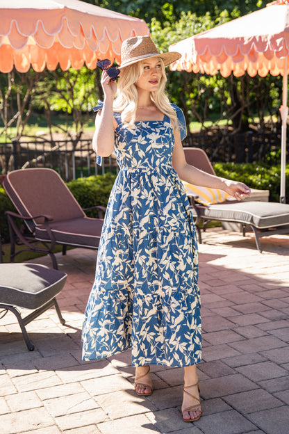 Woman in a blue floral dress standing outdoors under pink umbrellas.