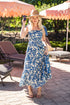 Woman in a blue floral dress standing outdoors under umbrellas.