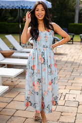 Woman in a floral dress standing on a patio with lounge chairs and an umbrella in the background.