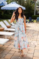 Woman in a floral dress standing on a patio with lounge chairs and umbrellas in the background.