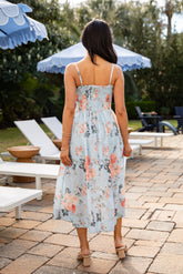 Woman in a floral dress walking on a patio with umbrellas and lounge chairs in the background.