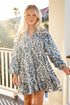 Woman in a blue patterned dress standing on a porch.