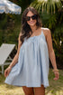 Woman in a light blue dress standing outdoors with greenery and a chair in the background