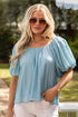 Woman wearing a light blue blouse and white pants outdoors.