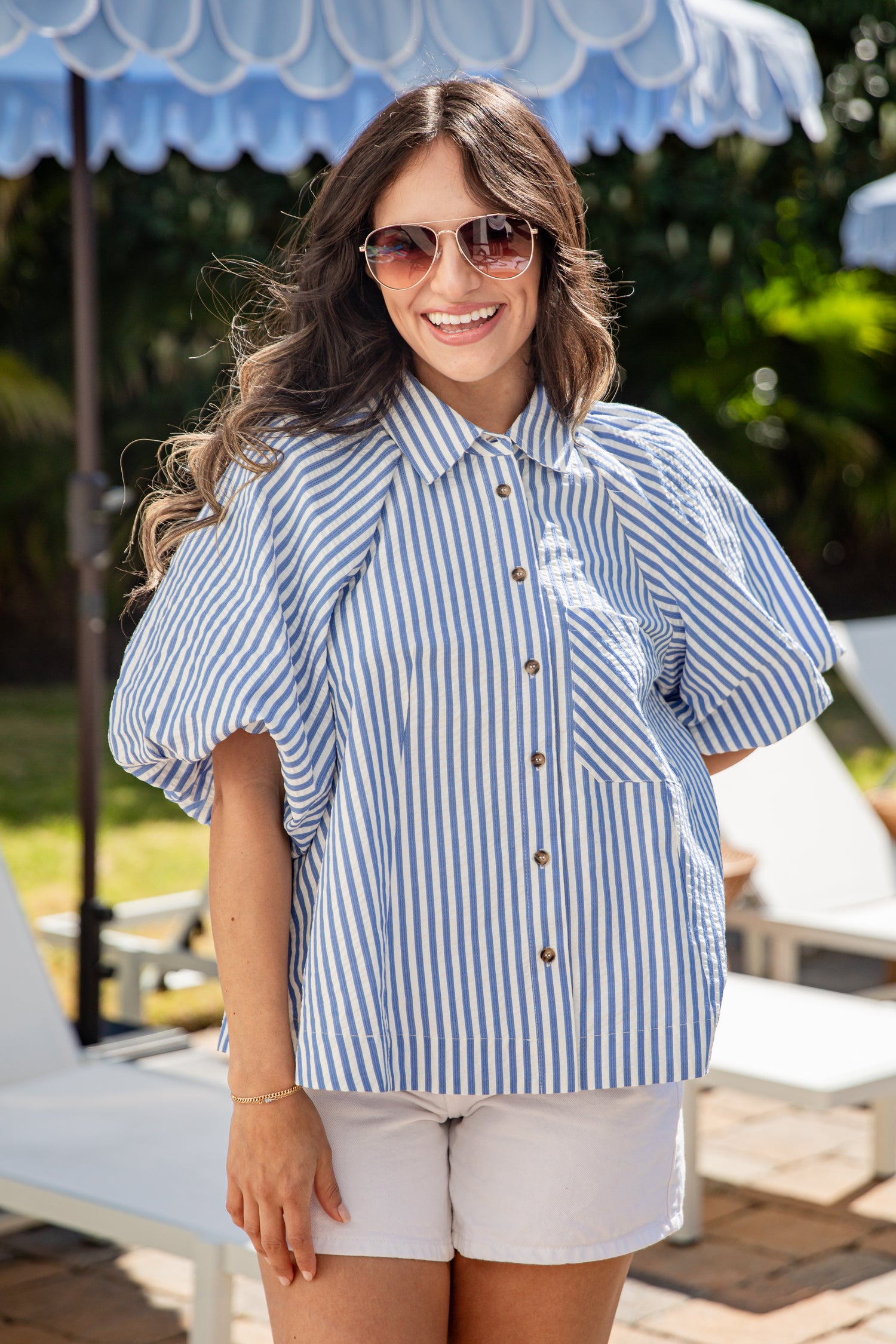 Woman wearing a blue and white striped shirt with sunglasses, standing under a blue umbrella.