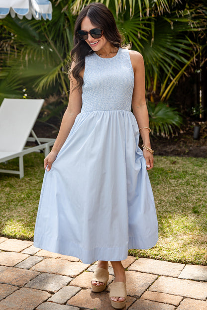 Woman in a light blue dress standing outdoors with palm trees in the background
