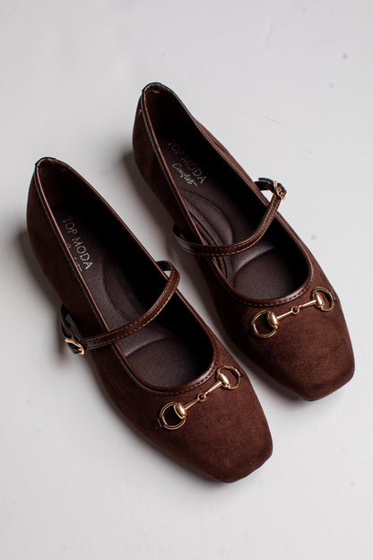 A pair of dark brown suede Mary Jane flats with gold-tone horsebit hardware and a thin strap, shown on a light gray background.
