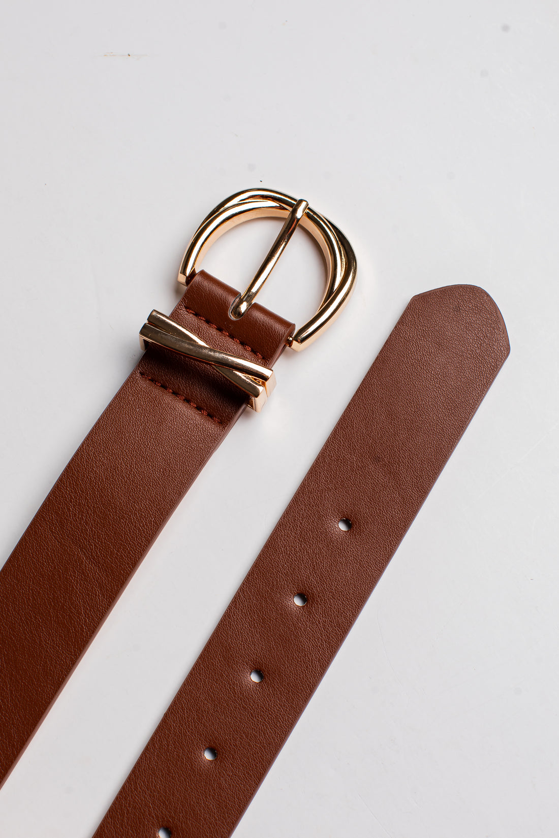 A close-up of a brown leather belt strap with a polished gold-tone buckle, laid diagonally on a clean white background.
