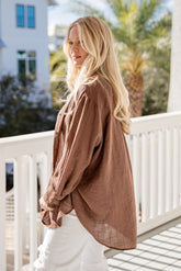 Woman wearing a brown oversized shirt on a balcony with a blurred background
