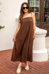 Woman wearing a brown slip dress standing on a brick patio.