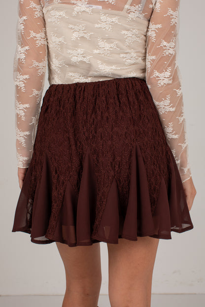 A dark brown lace and chiffon mini skirt worn by a model, paired with a sheer beige floral long-sleeve top, shown from the chest down against a plain light background.