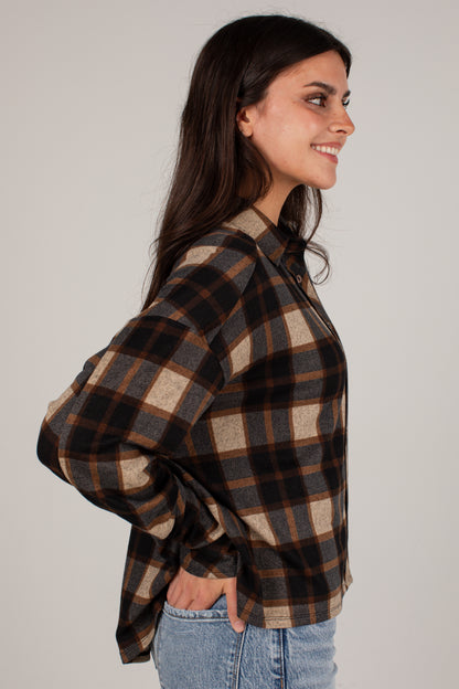 A woman wearing a brown, black, and beige plaid button-up shirt, shown in a side profile view against a plain light gray studio background.